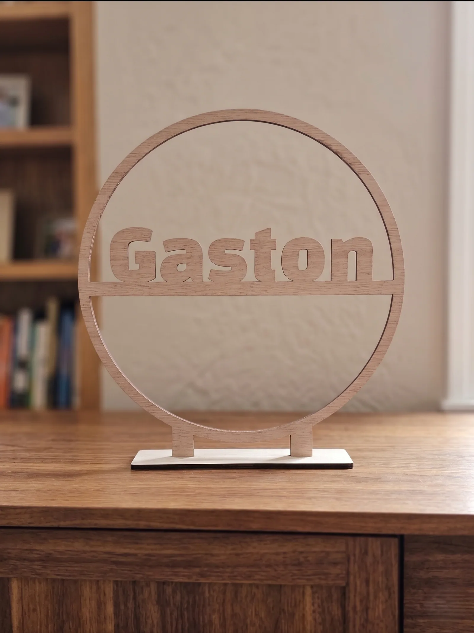Gepersonaliseerde houten naamcirkel op een dressoir in de woonkamer, met de naam Gaston uitgesneden in het hout